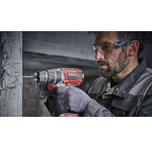 Muncitor care utilizează o mașină de găurit cu percuție cu acumulator Einhell pentru a găuri un perete de beton, purtând ochelari de protecție.
