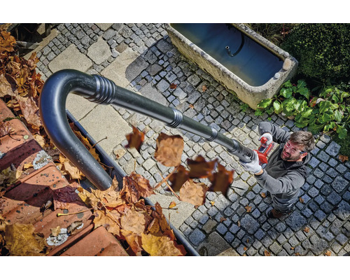 Un bărbat curăță jgheabul cu un accesoriu de suflantă pentru frunze cu acumulator de la nivelul solului.