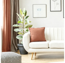 Un living luminos cu o canapea albă, o pernă decorativă ruginiu, o plantă de apartament într-un ghiveci și un taburet cu model geometric.