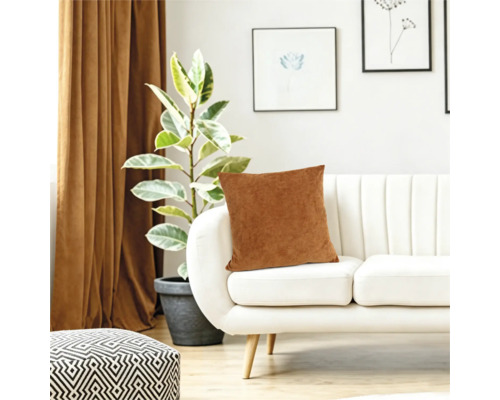 O pernă decorativă pe o canapea albă modernă în camera de zi, cu o plantă de apartament și perdele în fundal.