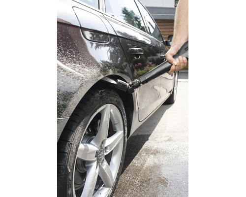O persoană curăță pasajul roții unui autoturism cu un aparat de spălat cu înaltă presiune și o duză Kärcher specială pentru întreținerea auto.