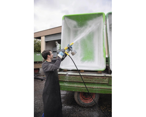 O persoană curăță un container mare în exterior cu un aparat de spălat cu presiune Karcher și duză de spumă.