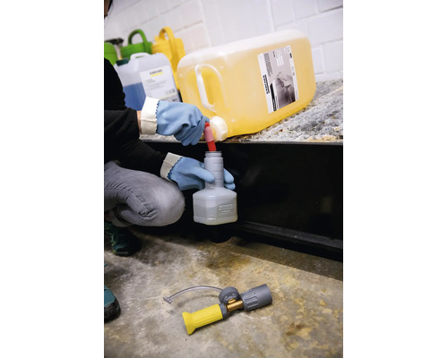 O persoană cu mănuși de protecție umple o sticlă mică Kärcher cu detergent dintr-un bidon mare Kärcher.