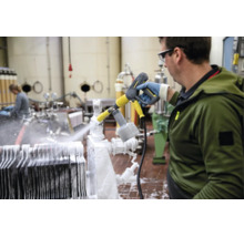 Un angajat curăță echipamente industriale într-o fabrică folosind un aparat de spălat cu presiune și un pulverizator de spumă Kärcher.