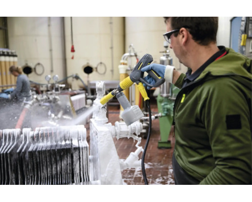Un angajat curăță echipamente industriale într-o fabrică folosind un aparat de spălat cu presiune și un pulverizator de spumă Kärcher.