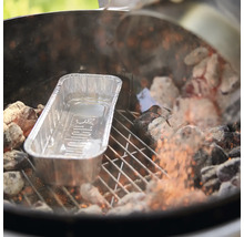 O tavă pentru grătar Weber din aluminiu pe un grătar cu cărbuni între cărbuni încinși.
