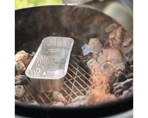 O tavă pentru grătar Weber din aluminiu pe un grătar cu cărbuni între cărbuni încinși.