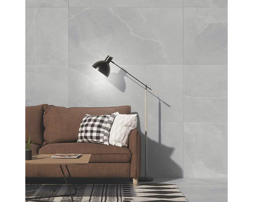 Living cu gresie mare cu aspect de piatră pe perete, canapea maro, măsuță de cafea și lampadar într-un design interior modern.