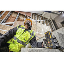 Muncitor cu telemetru laser Dewalt pe un șantier în construcție cu structură metalică și scară din beton.