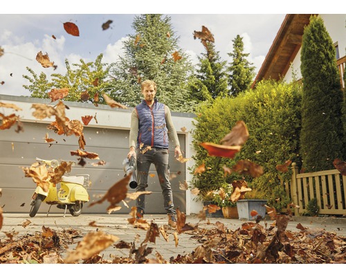 Bărbat folosind o suflantă de frunze pentru a îndepărta frunzele dintr-o curte.