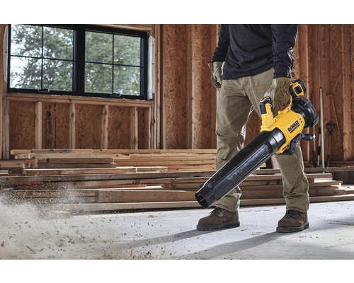 Un bărbat folosește o suflantă de frunze fără fir DeWalt galbenă și neagră pe un șantier.