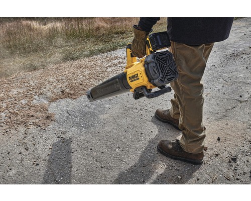 O persoană manevrează o suflantă de frunze fără fir DeWalt galbenă pe o suprafață neasfaltată.