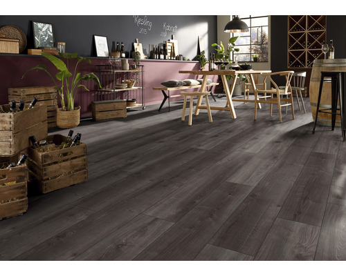 Interiorul unei camere cu podea laminată gri închis, masă din lemn cu scaune, rafturi și lăzi cu vin