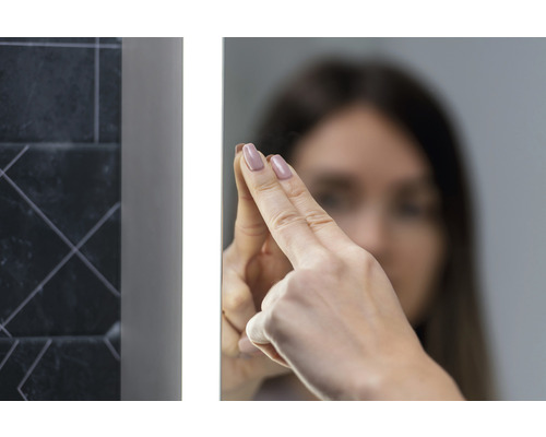 Femeie care atinge o oglindă de baie iluminată