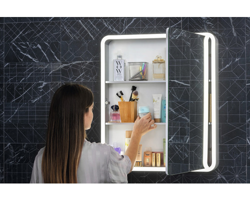 Femeie în fața unui dulap cu oglindă cu iluminare în baie