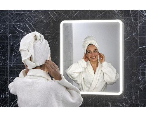 Femeie cu prosop pe cap în fața unei oglinzi de baie iluminate