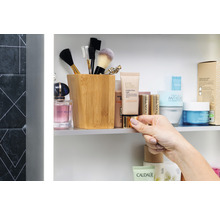 Scenă de baie cu produse cosmetice, pensule de machiaj într-un recipient și o mână care ține o cutie.