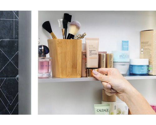 Scenă de baie cu produse cosmetice, pensule de machiaj într-un recipient și o mână care ține o cutie.