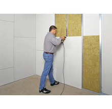 Un bărbat fixează plăci de gips-carton pe un perete cu izolație.