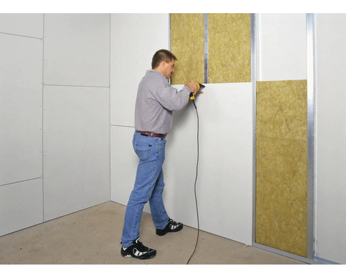 Un bărbat fixează plăci de gips-carton pe un perete cu izolație.