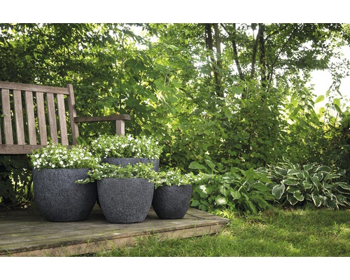 Trei jardiniere întunecate din plastic plantate pe o terasă de lemn într-o grădină.