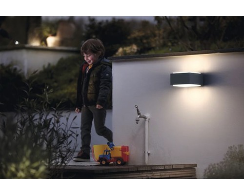 Scenă cu un băiat în fața unei case cu o lampă de perete dreptunghiulară.