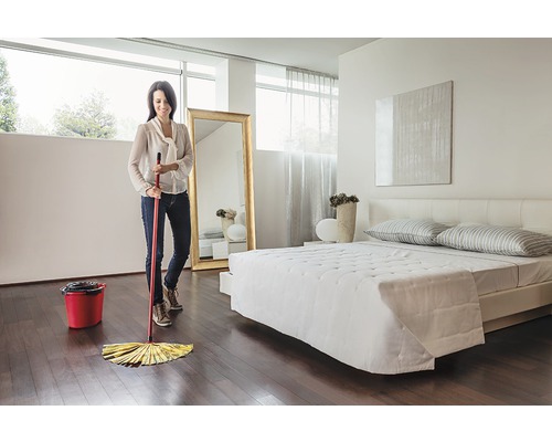 Femeie șterge podeaua de lemn cu mopul într-un dormitor