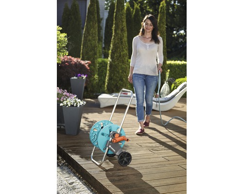 Scenă de grădină cu o femeie care folosește un furtun de grădină pe o bobină de cărucior cu furtun pe o terasă din lemn.