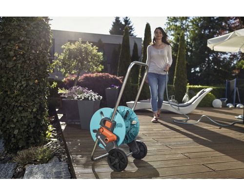 Cărucior pentru furtun Gardena pe o terasă de lemn cu o femeie ținând un furtun de grădină