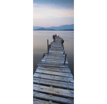 Un ponton lung din lemn vechi duce într-o apă cu munți în fundal.