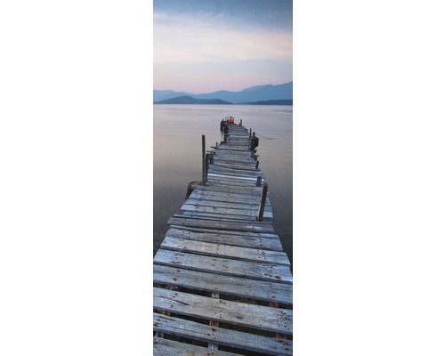 Un ponton lung din lemn vechi duce într-o apă cu munți în fundal.