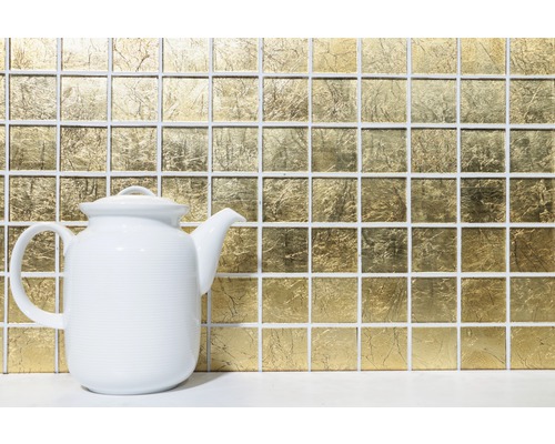 Plăci de mozaic de culoare aurie în fundal, cu un ceainic alb în prim-plan