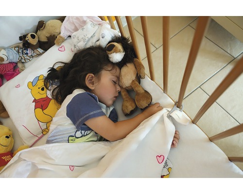 Un copil dormind cu un leu de pluș într-un pătuț cu lenjerie de pat Winnie the Pooh.