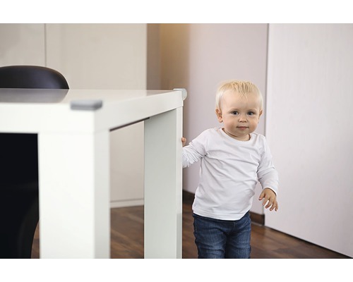 Copil mic stând lângă o masă cu protecții de colț.