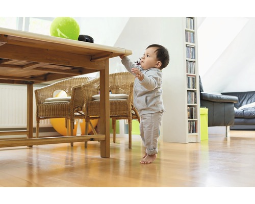 Copil mic sprijinindu-se de o masă de lemn într-o cameră de zi luminoasă.