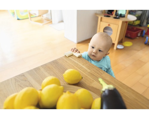 Copil mic stând la o masă cu protecție pentru colțuri, lămâi și o vânătă