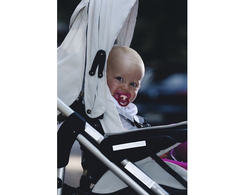Un bebeluș cu suzetă stă într-un cărucior.