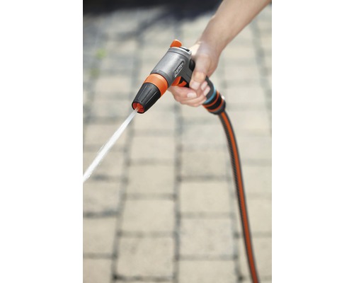 O mână ține un pistol de pulverizare pentru grădină cu un jet de apă.