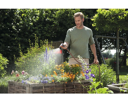 Un bărbat udă flori într-un strat înălțat cu un furtun de grădină