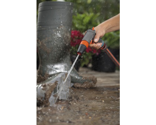 O persoană curăță o lopată de grădină cu un duș de grădină lângă cizme de cauciuc.