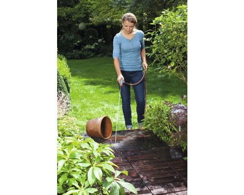 Femeie udând o terasă și o vază de flori în grădină cu un furtun de grădină.