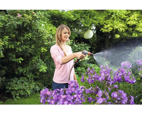 Femeie udând flori cu un furtun de grădină în grădină.