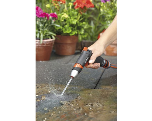 O persoană folosește un pistol de pulverizare de grădină pentru a curăța o terasă în fața unor ghivece plantate.