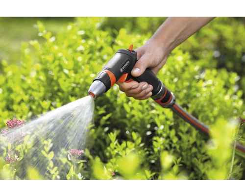 O mână ține un pistol de stropit marca Gardena, care pulverizează apă pe plante.