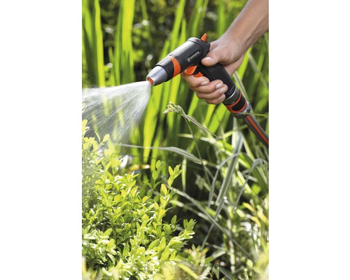 O mână ține un pulverizator de grădină care stropește plantele cu apă.