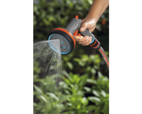 O persoană ține un pulverizator multifuncțional de grădină Gardena care pulverizează apă.