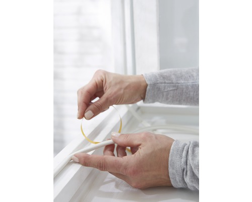 O persoană fixează bandă de etanșare pe un cadru de fereastră.