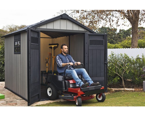 Bărbat conduce tractorul de gazon într-o magazie de grădină pentru întreținerea gazonului.