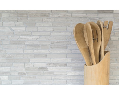 Ustensile de bucătărie din lemn într-un suport în fața unui perete de piatră