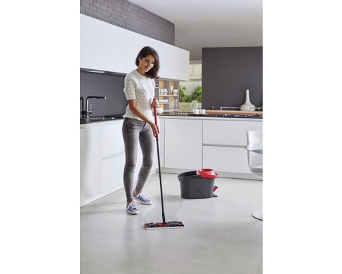 Femeie șterge podeaua bucătăriei cu un mop, găleată în fundal